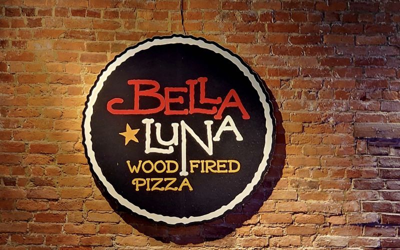 The Bella Luna Wood-Fired Pizza sign on an exposed brick wall inside the downtown Harrisonburg restaurant